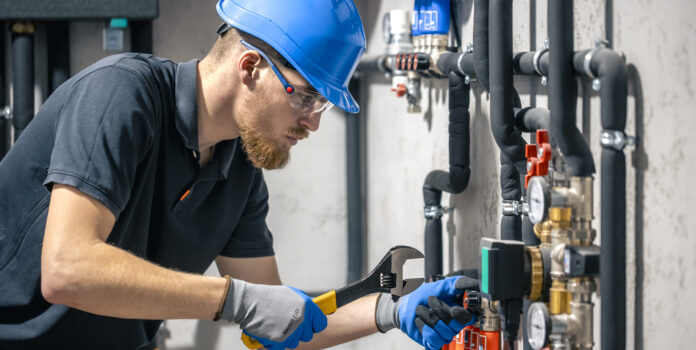 A man installs a heating system in a house and checks the pipes with a wrench.